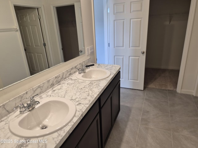 bathroom with tile patterned floors, double vanity, a walk in closet, and a sink