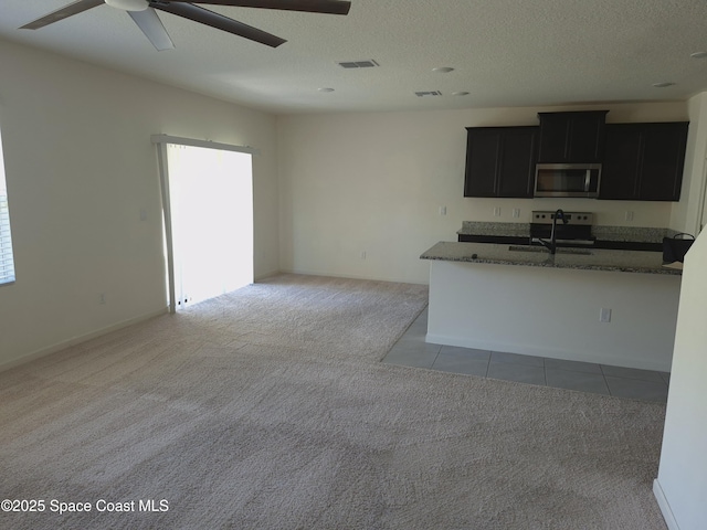 kitchen featuring dark cabinetry, visible vents, ceiling fan, stainless steel appliances, and light carpet