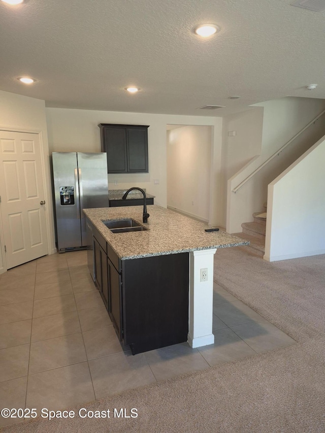 kitchen featuring stainless steel fridge with ice dispenser, light stone countertops, a center island with sink, light carpet, and a sink