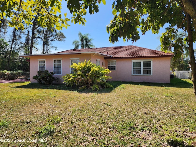 rear view of property with a yard, a tile roof, stucco siding, and fence