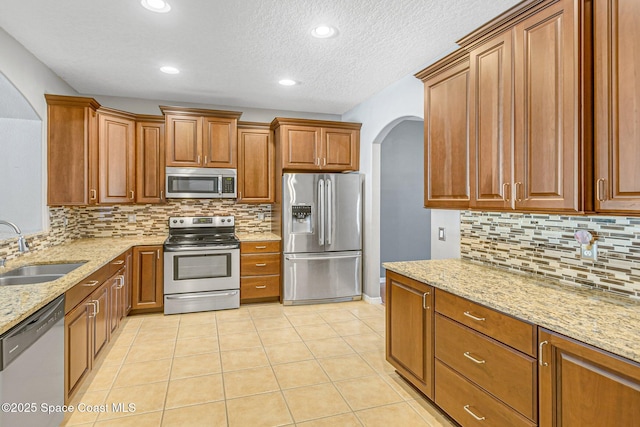 kitchen featuring a sink, brown cabinetry, arched walkways, and stainless steel appliances