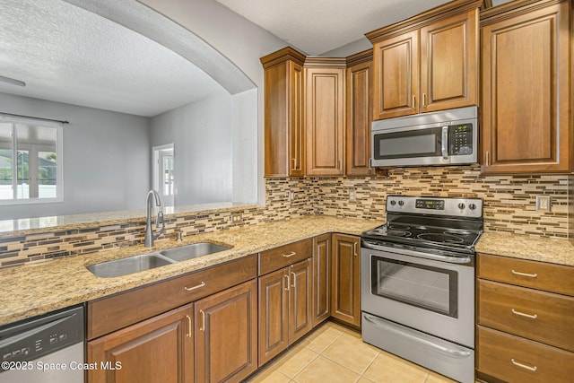 kitchen with a sink, backsplash, appliances with stainless steel finishes, light tile patterned floors, and light stone countertops