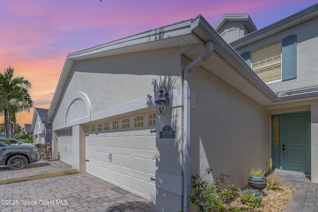 view of property exterior with stucco siding, decorative driveway, and a garage