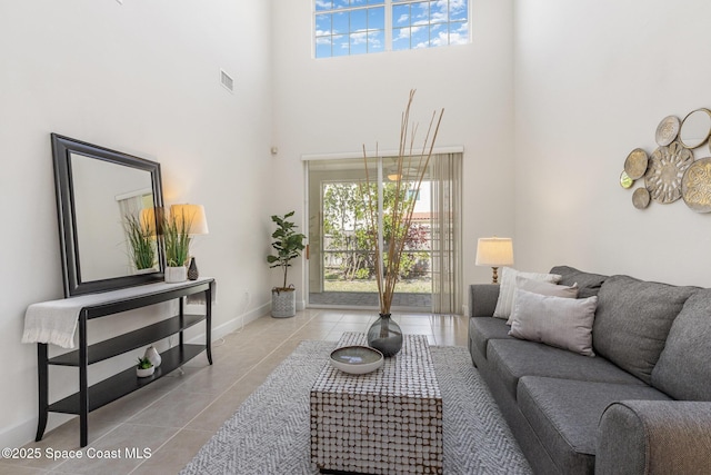 living room featuring tile patterned flooring, visible vents, a high ceiling, and baseboards