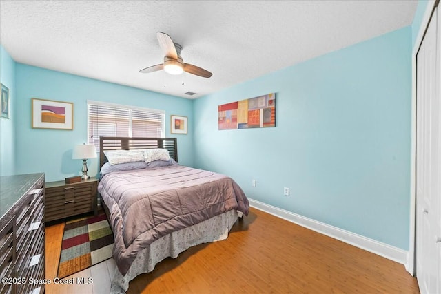 bedroom with a textured ceiling, wood finished floors, a closet, baseboards, and ceiling fan