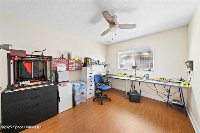 home office featuring baseboards, light wood-style flooring, a textured ceiling, and ceiling fan