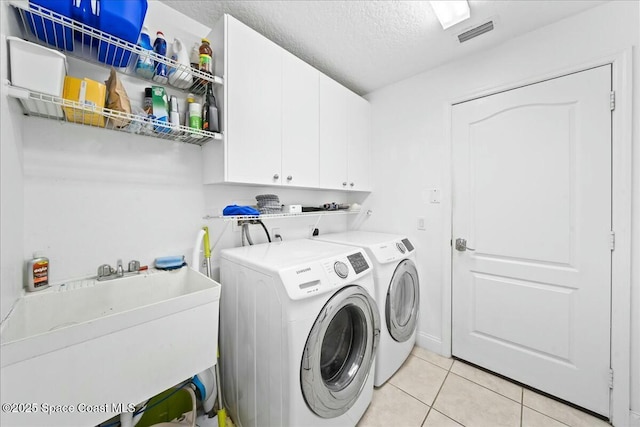 washroom featuring visible vents, a sink, washing machine and dryer, cabinet space, and light tile patterned floors