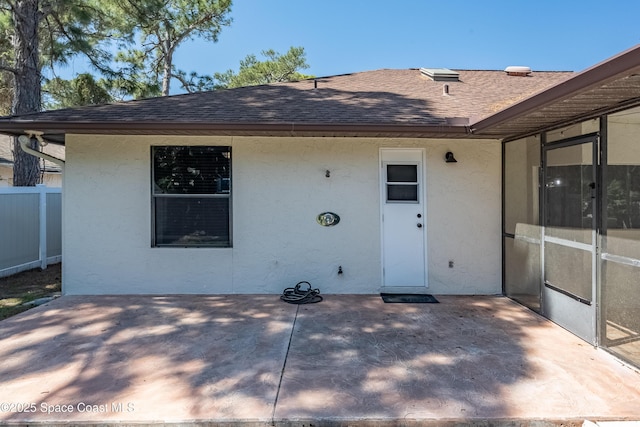 rear view of property featuring stucco siding, fence, roof with shingles, and a patio area