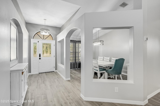 entryway with visible vents, arched walkways, light wood-style floors, baseboards, and vaulted ceiling