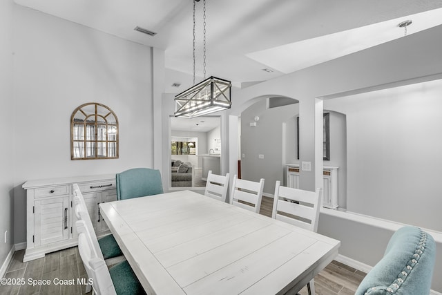 dining room with arched walkways, wood finished floors, visible vents, and baseboards