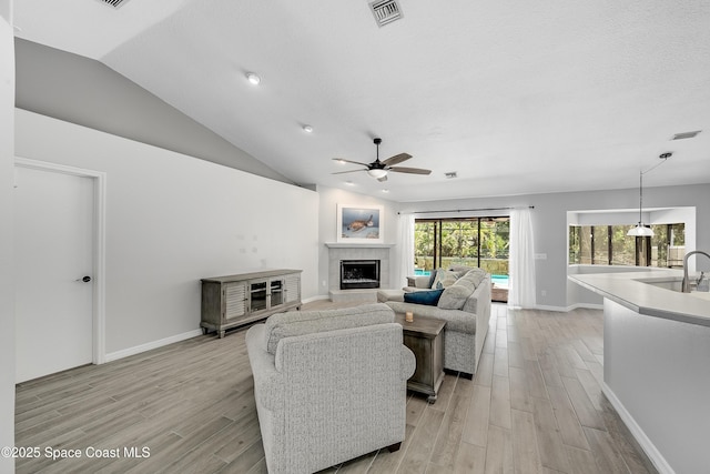 living area with visible vents, a fireplace, light wood-style floors, and vaulted ceiling