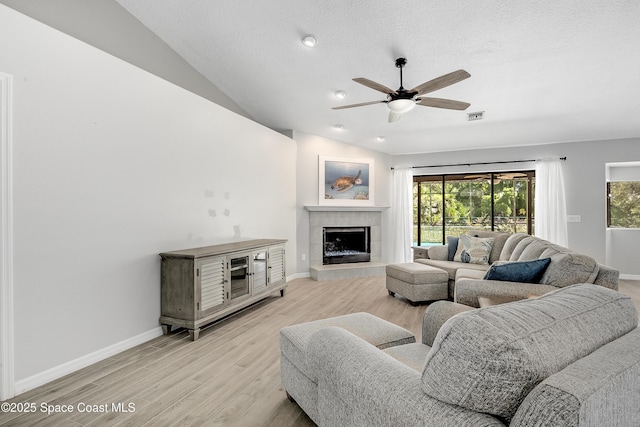 living room featuring baseboards, visible vents, a fireplace, vaulted ceiling, and light wood-type flooring