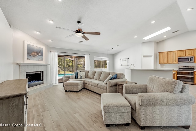 living area with a tiled fireplace, lofted ceiling, light wood-style flooring, a textured ceiling, and a ceiling fan