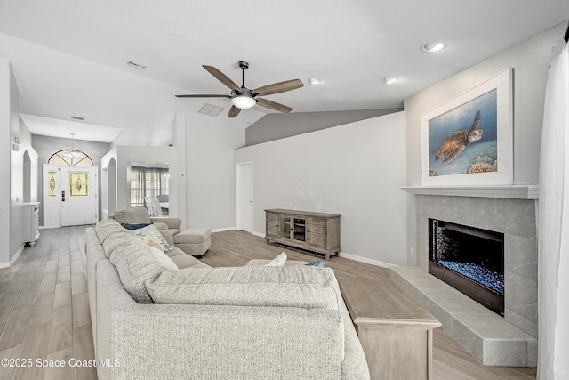 living area featuring visible vents, ceiling fan, vaulted ceiling, light wood-style floors, and a tiled fireplace