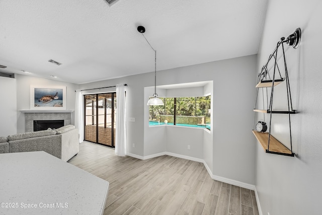 dining space with visible vents, a textured ceiling, wood finished floors, baseboards, and a tile fireplace