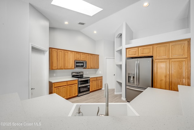 kitchen with light wood finished floors, lofted ceiling with skylight, light countertops, stainless steel appliances, and a sink