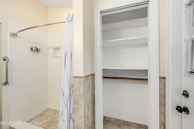 bathroom featuring a wainscoted wall, tile walls, a walk in closet, and a shower stall