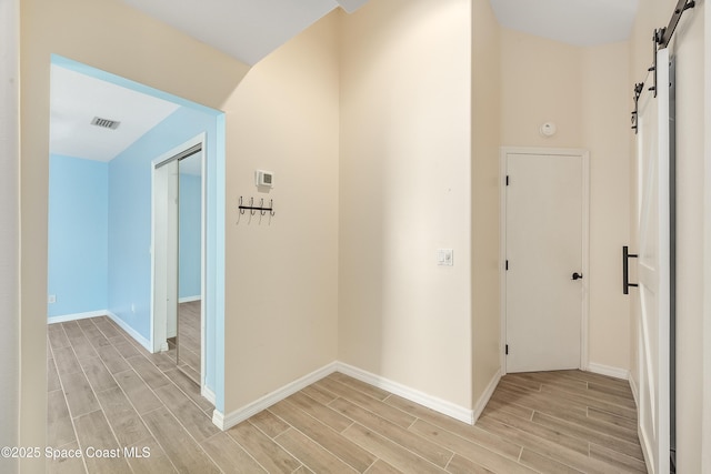 corridor featuring a barn door, baseboards, visible vents, and wood finish floors