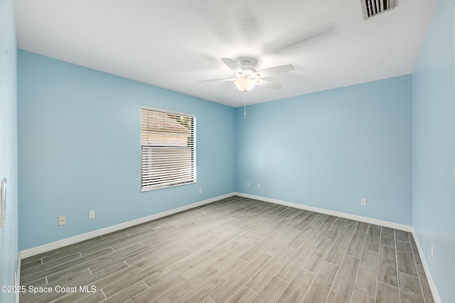 spare room with ceiling fan, visible vents, baseboards, and wood finished floors