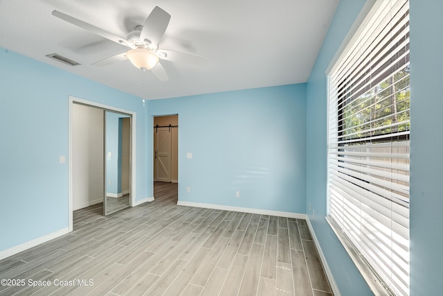 unfurnished bedroom featuring a barn door, light wood-style flooring, baseboards, and visible vents