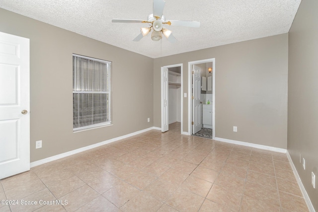 unfurnished bedroom featuring ceiling fan, a spacious closet, baseboards, and a textured ceiling