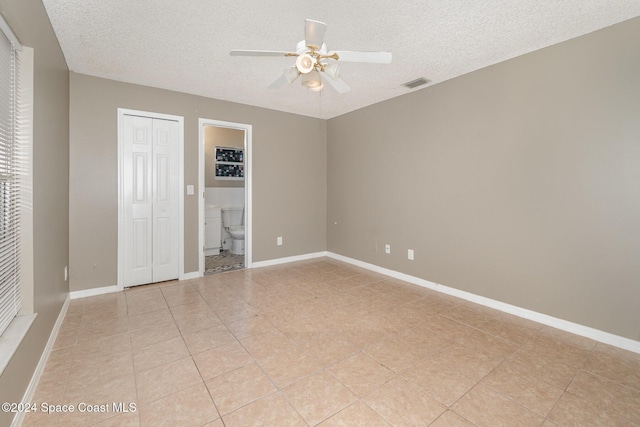 unfurnished bedroom featuring baseboards, visible vents, ceiling fan, ensuite bathroom, and a textured ceiling