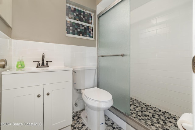 bathroom featuring toilet, a tile shower, tile walls, wainscoting, and vanity