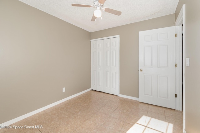 unfurnished bedroom featuring a ceiling fan, a textured ceiling, a closet, light tile patterned flooring, and baseboards