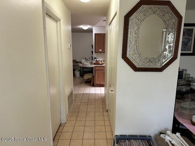 hallway with a textured ceiling and light tile patterned flooring