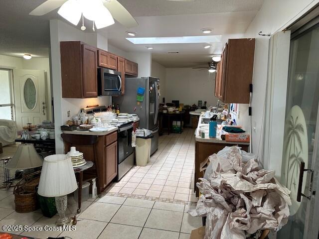 kitchen with light tile patterned flooring, a ceiling fan, brown cabinets, and appliances with stainless steel finishes