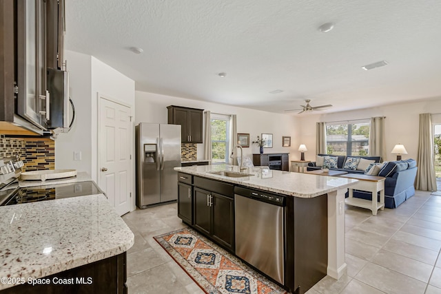 kitchen featuring a sink, stainless steel appliances, dark brown cabinetry, open floor plan, and tasteful backsplash