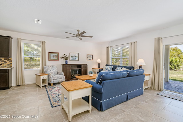 living area featuring a glass covered fireplace, light tile patterned flooring, a ceiling fan, and visible vents