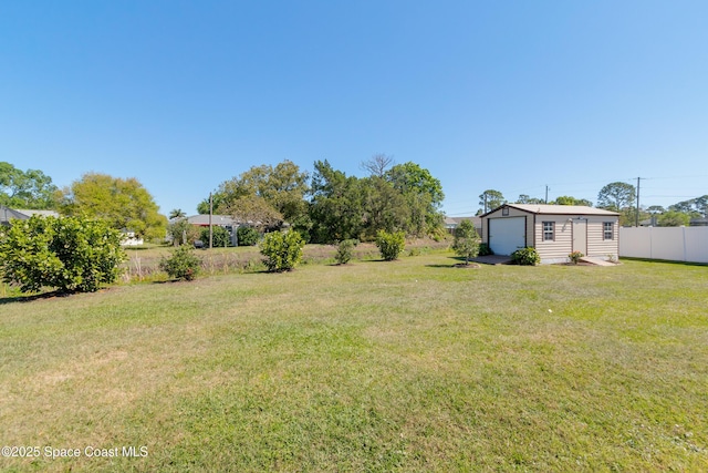 view of yard with a detached garage, an outbuilding, and fence