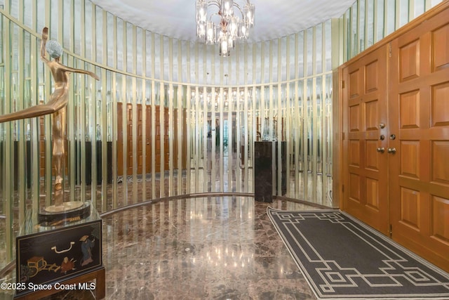 foyer entrance featuring a chandelier, marble finish floor, and wallpapered walls