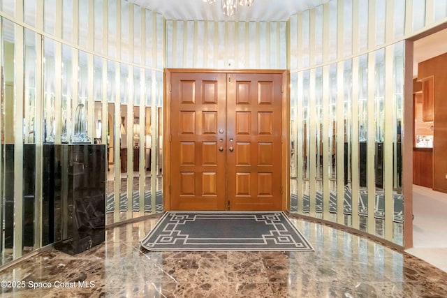 foyer entrance featuring wallpapered walls, a notable chandelier, and marble finish floor