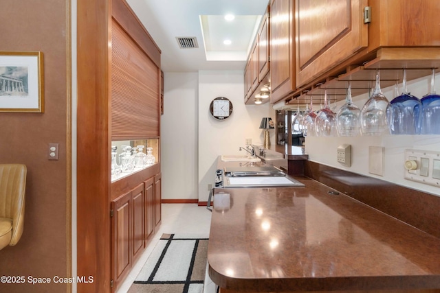 kitchen featuring baseboards, visible vents, a tray ceiling, a sink, and brown cabinets