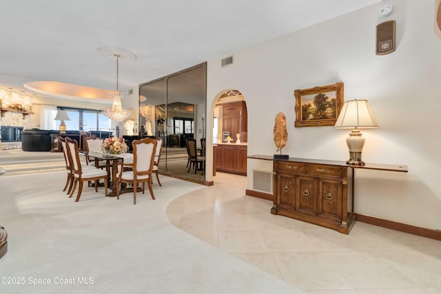 dining space with light tile patterned floors, visible vents, arched walkways, and a chandelier