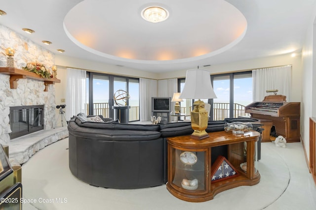 living room featuring a stone fireplace, a tray ceiling, and carpet floors