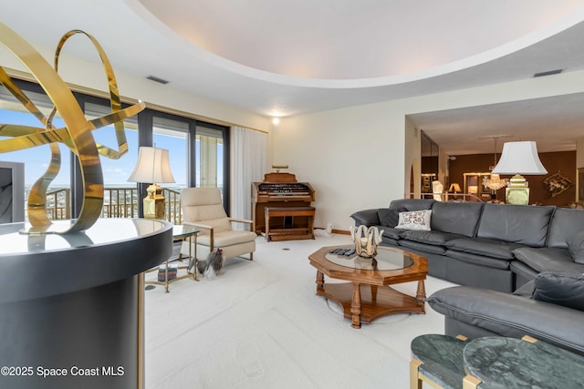 living area with visible vents, a raised ceiling, an inviting chandelier, baseboards, and light colored carpet