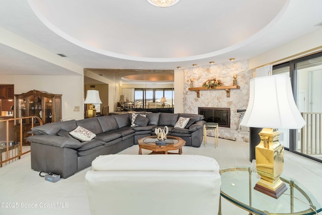 living area with a stone fireplace, visible vents, and a tray ceiling