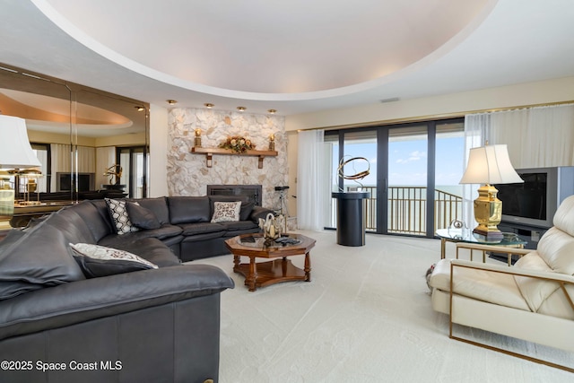 living area featuring a raised ceiling, a fireplace, and light colored carpet