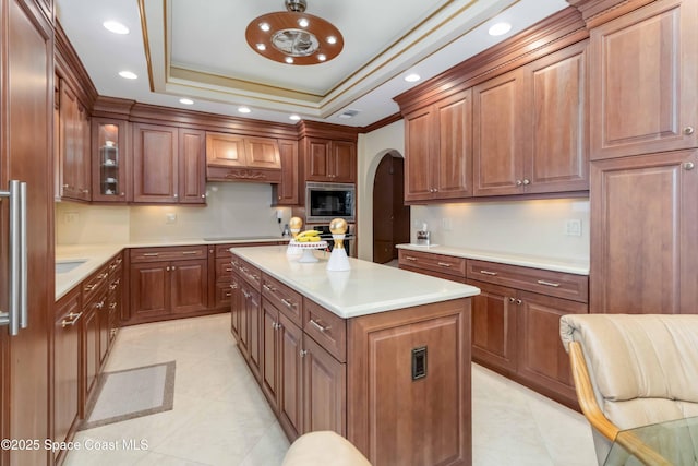 kitchen with premium range hood, stainless steel microwave, a center island, arched walkways, and a raised ceiling