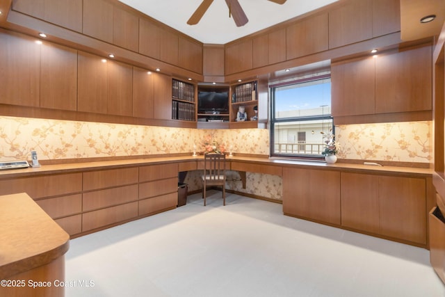 kitchen featuring a ceiling fan, modern cabinets, built in desk, and wallpapered walls