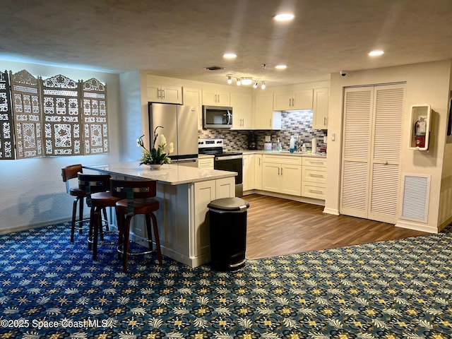 kitchen featuring visible vents, stainless steel appliances, white cabinetry, backsplash, and a center island