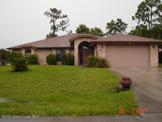 single story home featuring a front lawn, an attached garage, brick siding, and driveway