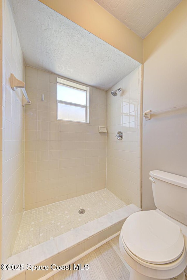 bathroom featuring a textured ceiling, toilet, wood finished floors, and a tile shower