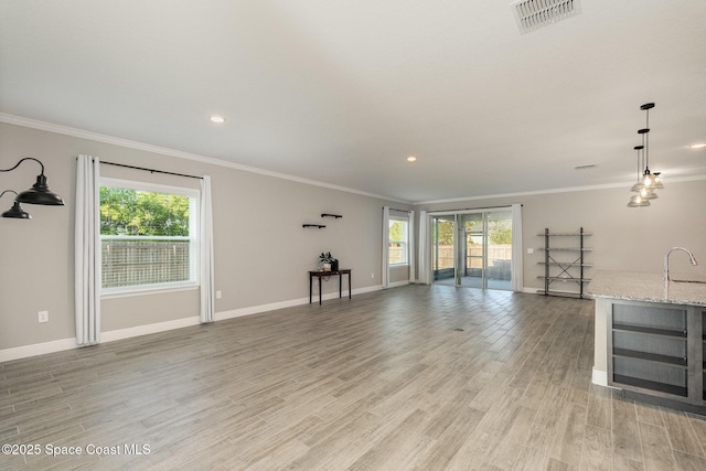 unfurnished living room featuring visible vents, plenty of natural light, light wood-type flooring, and a sink