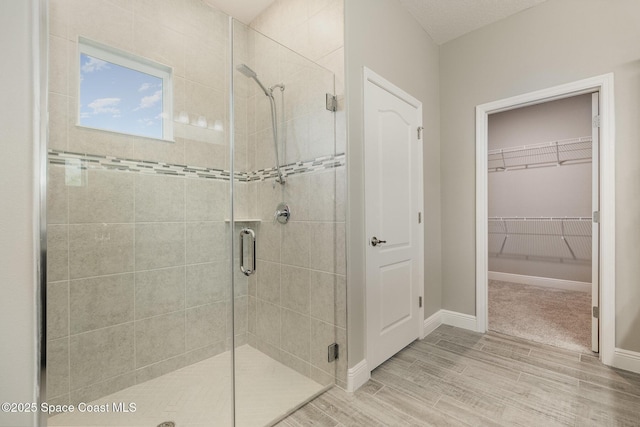 full bath featuring baseboards, wood finished floors, a stall shower, and a spacious closet