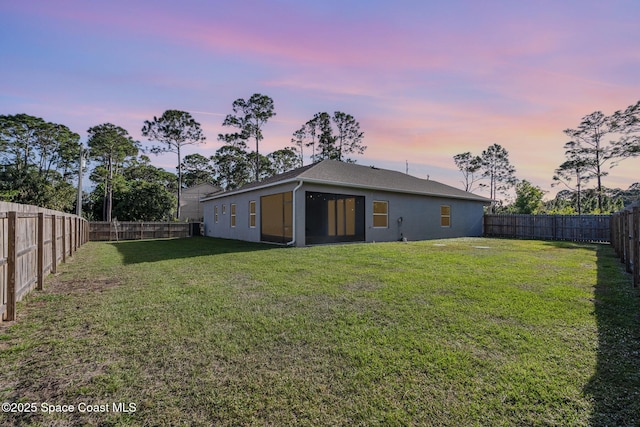 back of house at dusk featuring a yard, a fenced backyard, and stucco siding