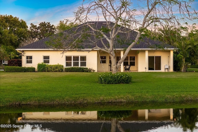 rear view of property featuring stucco siding, a yard, and a water view